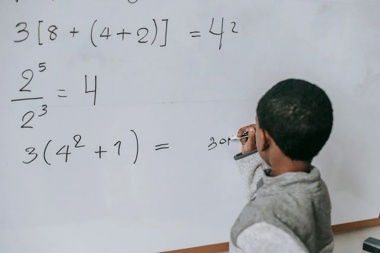 Focused child solving equations on a whiteboard, showcasing education and problem-solving skills.