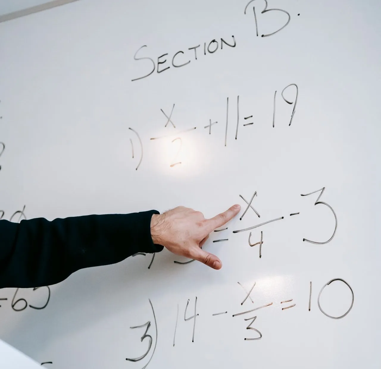 Close-up of an instructor's hand solving math equations on a whiteboard during a lesson.